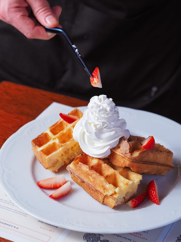 Close-up of waffles with strawberries and whipped cream on a plate.